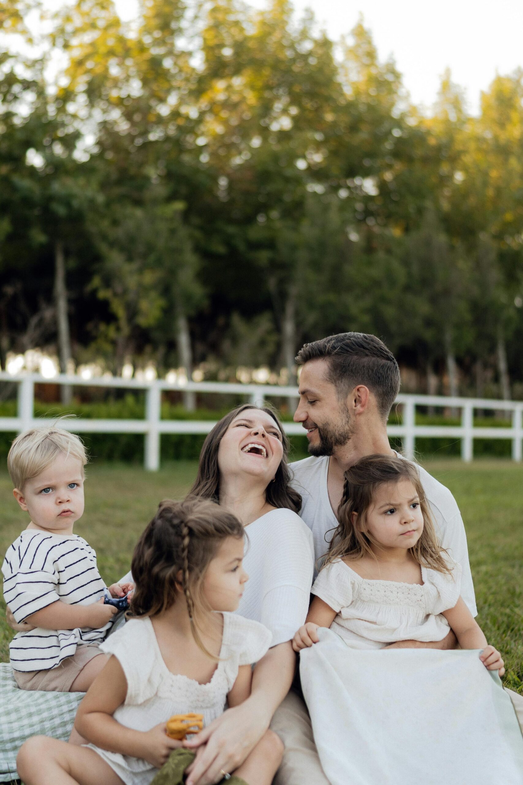 Family of five laughing and enjoying a sunny day on the grass with a forest background.